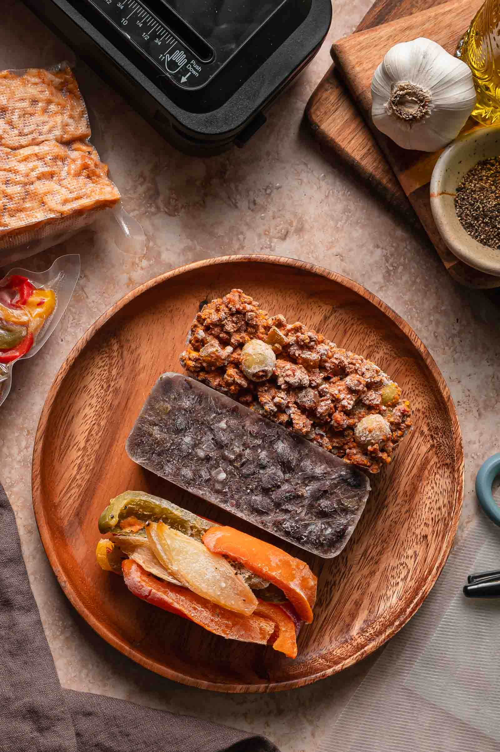 Three frozen meal portions, including a peppers and onions mix, picadillo and Cuban black beans, are arranged on a wooden plate to be reheated.