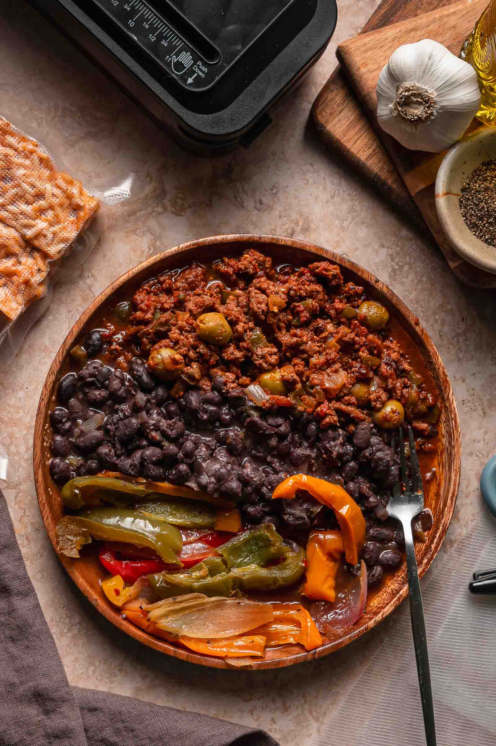 Wooden plate with Cuban picadillo, black beans, and peppers and onions.