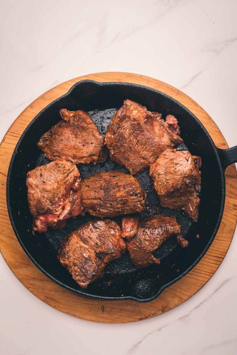 Pieces of seasoned meat of seared meat being browned in a cast iron skillet.