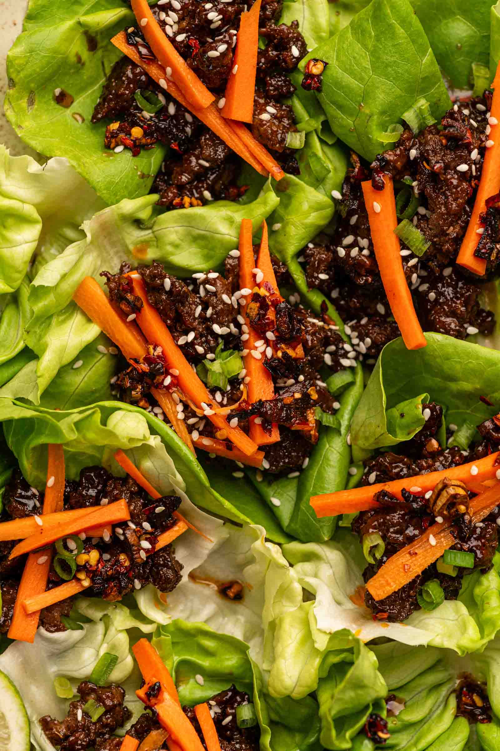 Butter lettuce wraps filled with minced lamb, shredded carrots, green onions, and sprinkled with sesame seeds.
