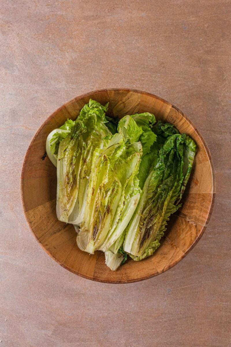 Grilled romaine halves, charred at the edges and still bright green, piled in a wooden salad bowl.