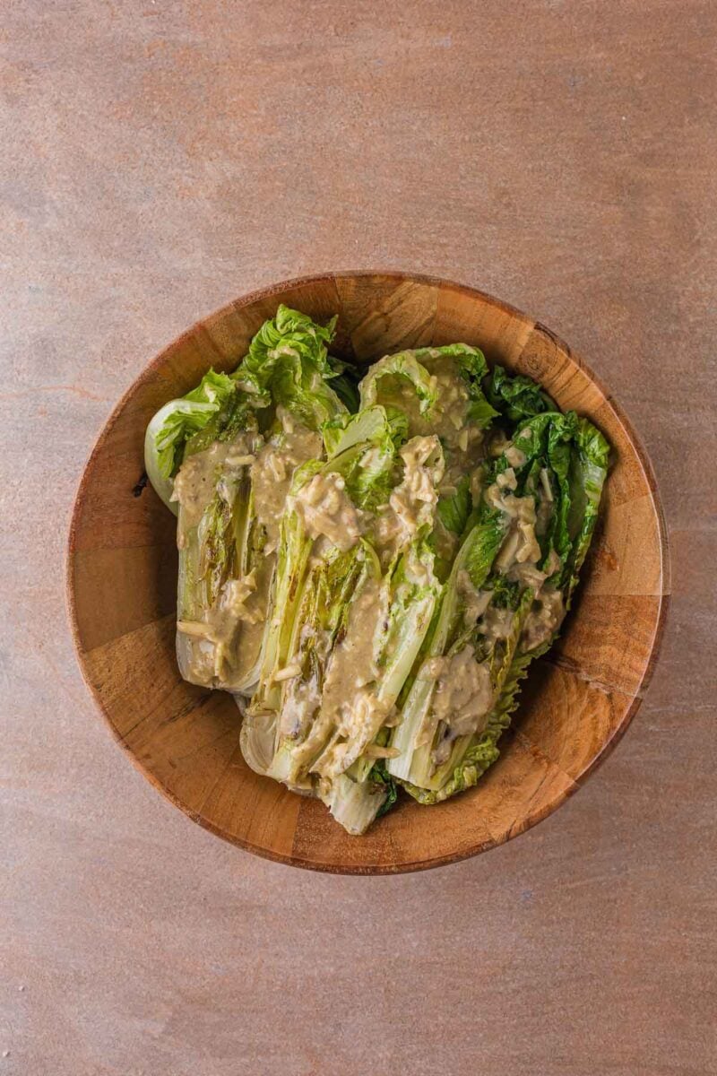 Creamy anchovy garlic Caesar dressing spooned over the grilled romaine halves in the wooden bowl.