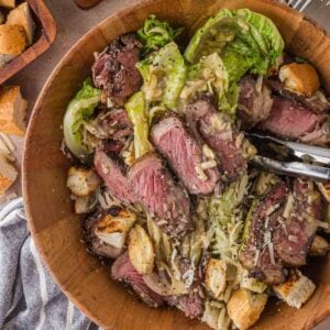 The full bowl of grilled steak Caesar salad with tongs, the grilled romaine spooned with dressing rather than tossed.