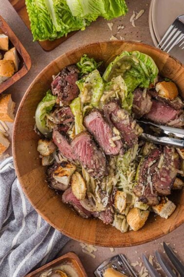 The full bowl of grilled steak Caesar salad with tongs, the grilled romaine spooned with dressing rather than tossed.