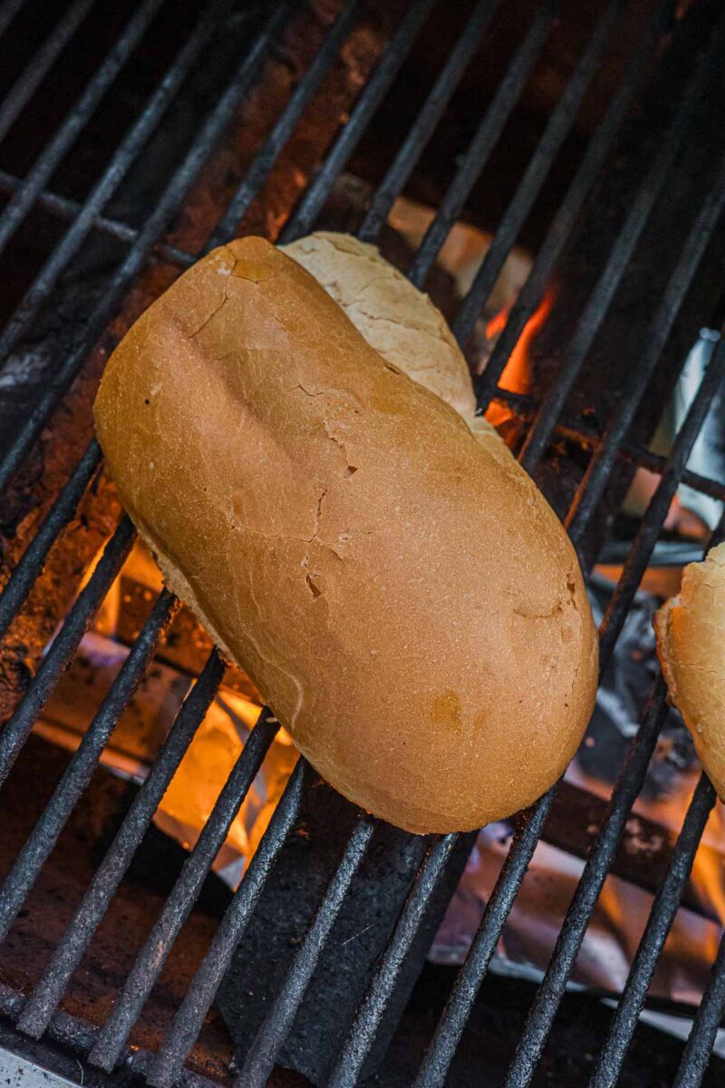 Oiled slices of Italian bread toasting on the grill grate over an open flame to become the grilled croutons.