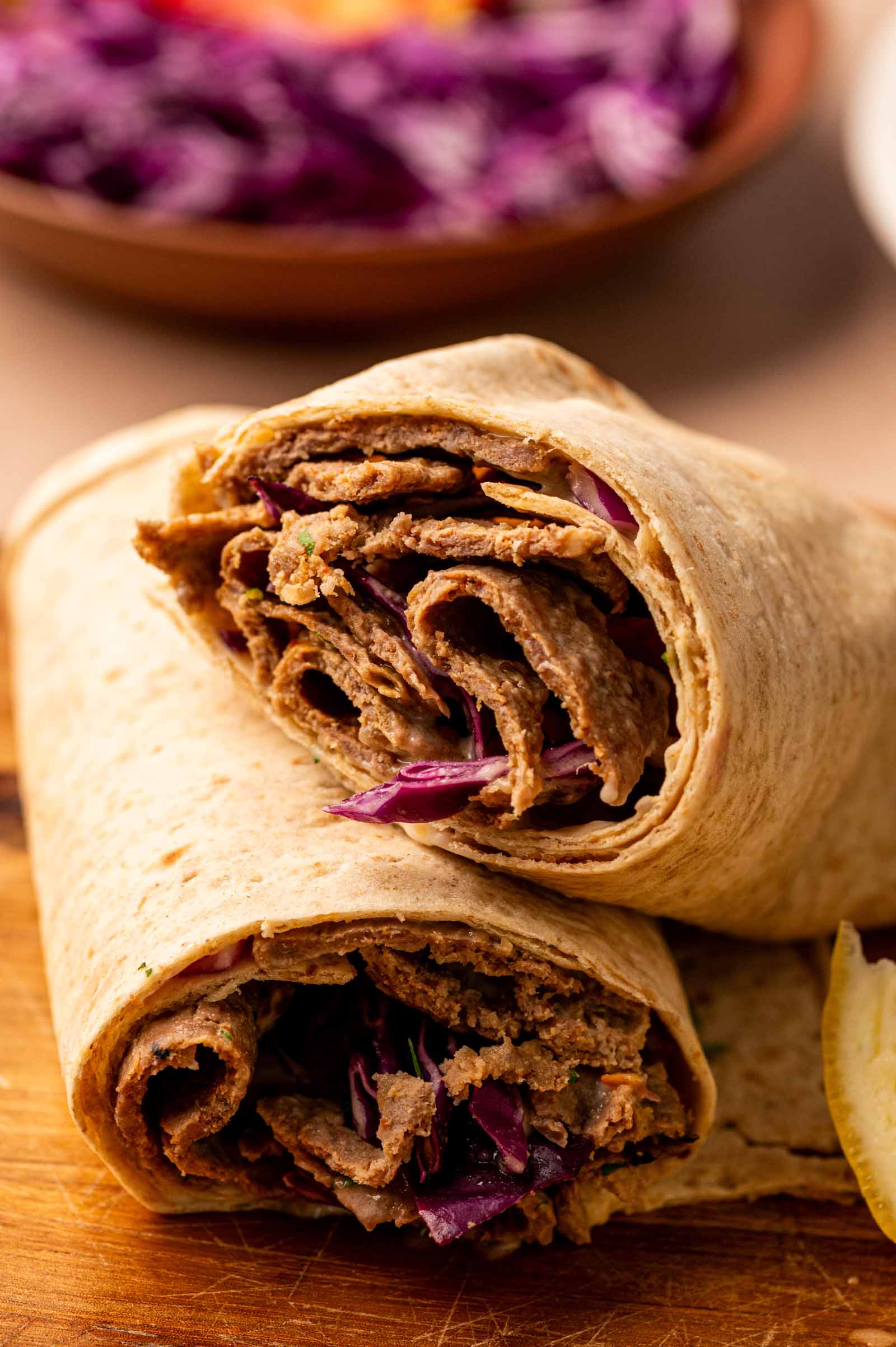 Two halved diner kebab wraps filled with sliced lamb and purple cabbage, placed on a wooden surface with a lemon wedge nearby.