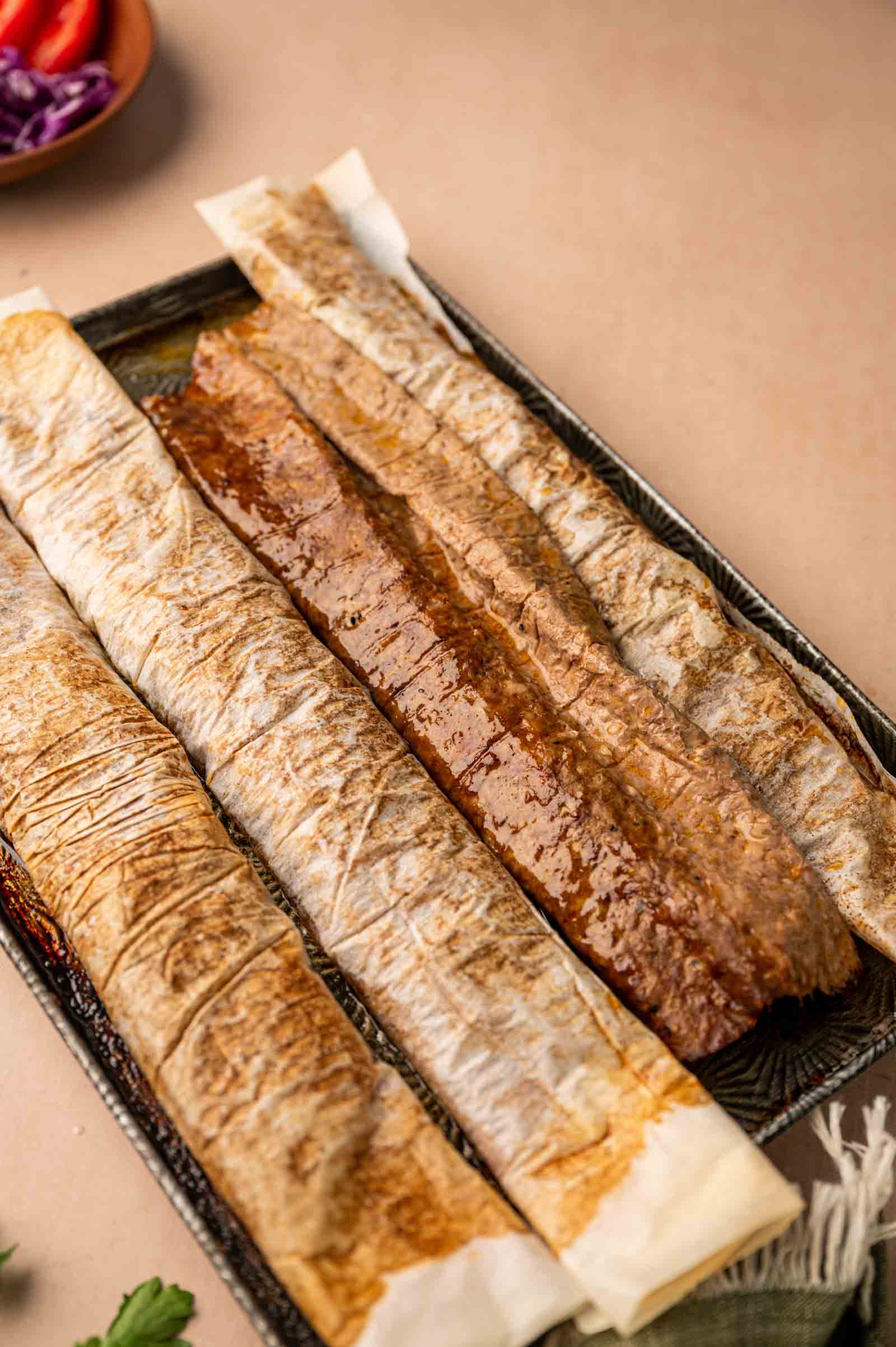 Lamb doner rollups fresh from the oven, showing one removed from the parchment paper while the others are still in it.