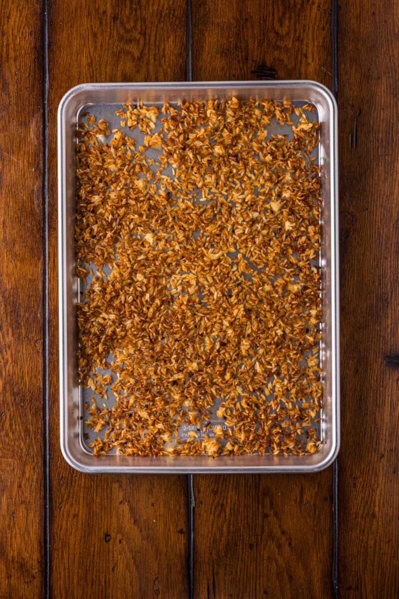 A baking tray filled with evenly spread, toasted golden-brown crispy rice sits on a wooden surface.