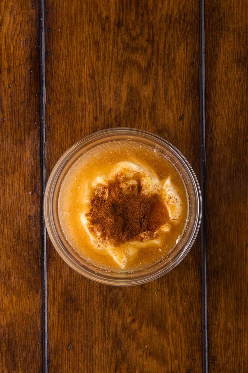 A glass bowl with a mixture of mayo, paprika, rice vinegar, and sugar sits on a wooden table.