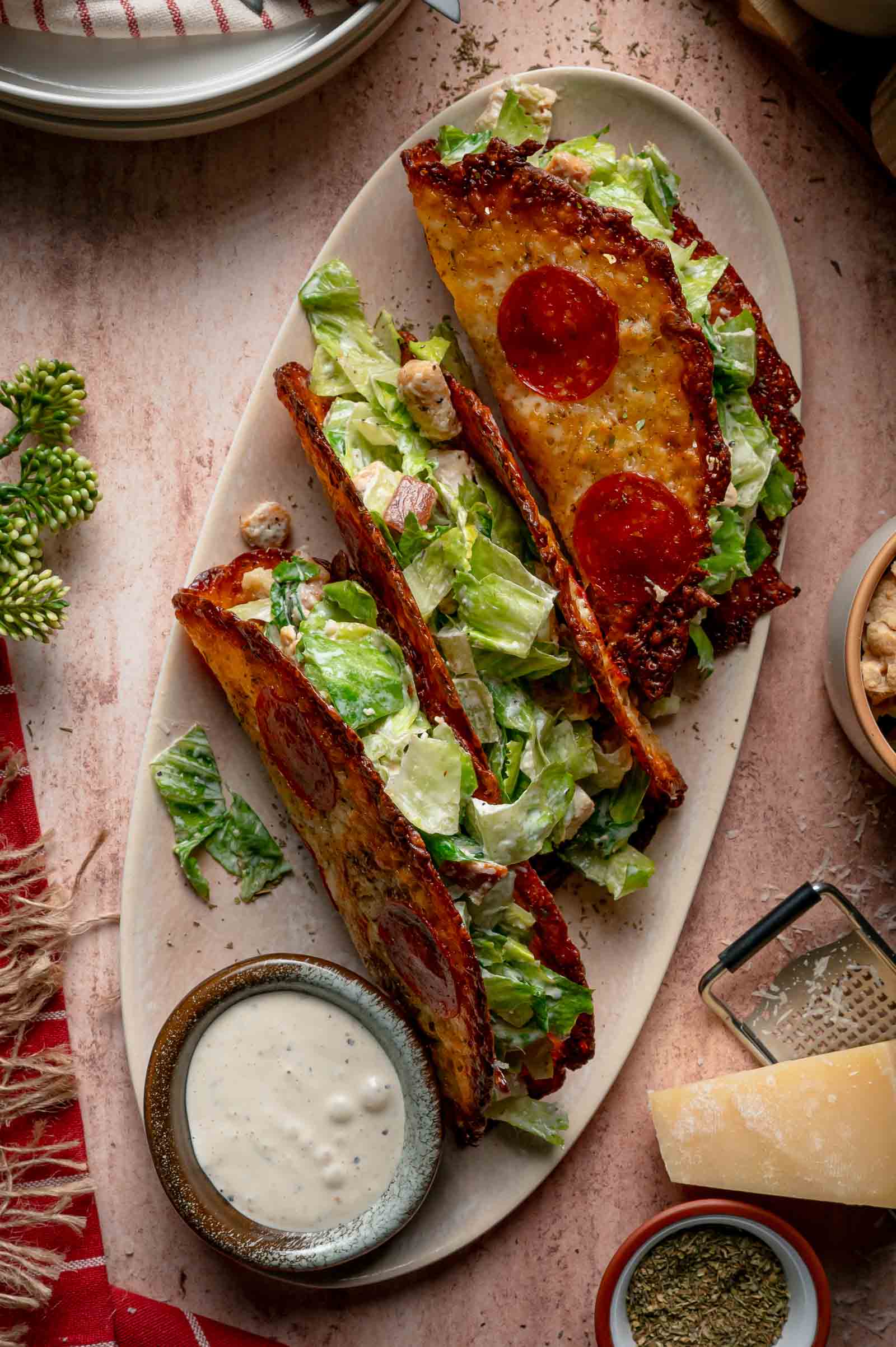 Three pepperoni pizza Caesar salad wraps on an oval plate, served with a side of creamy dressing.