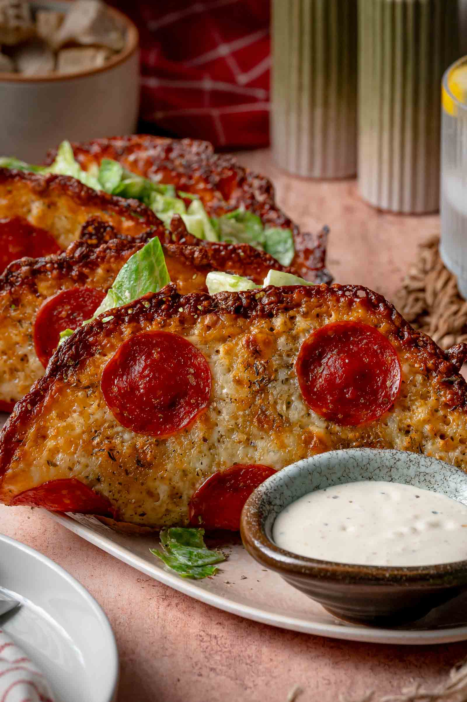 Three pizza wraps with pepperoni, filled with Caesar salad, served on a plate with a small bowl of Caesar dressing.