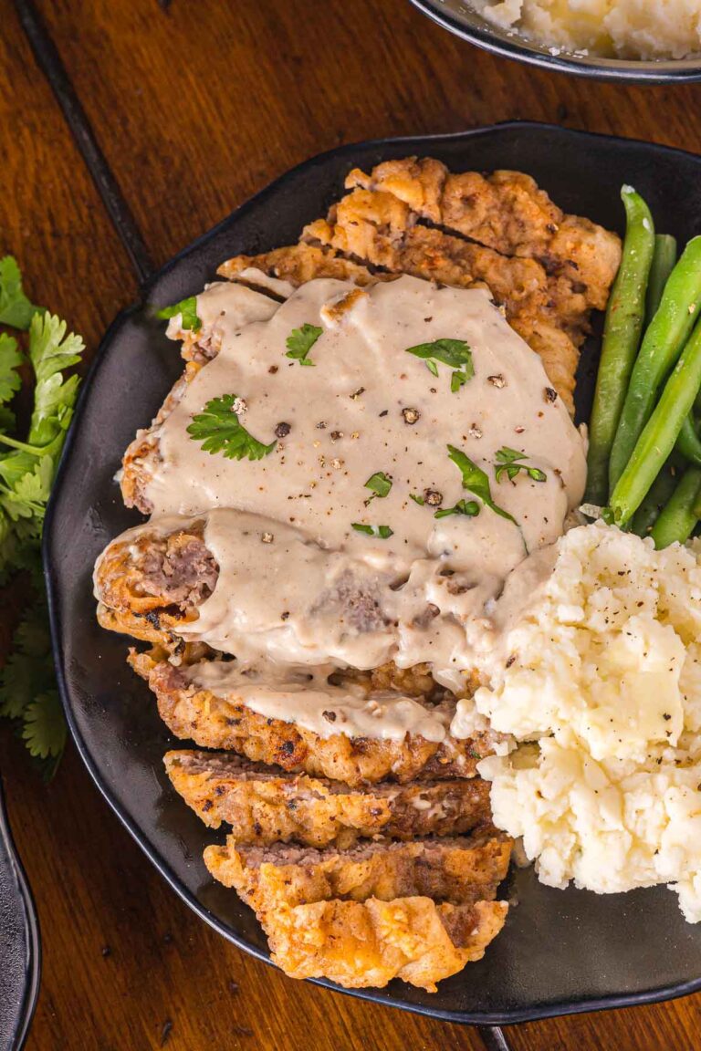 A plate with chicken fried steak topped with creamy gravy, served with mashed potatoes and green beans.