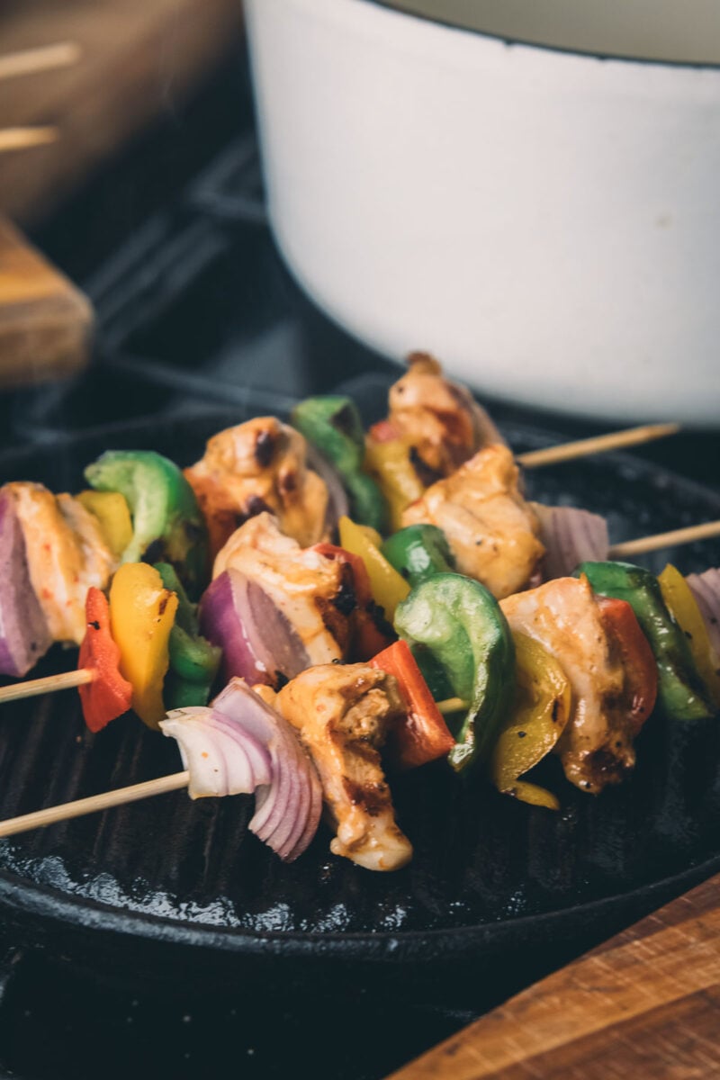 Chipotle chicken and vegetable skewers with red onion, bell peppers, and grilled chicken pieces cooking on a grill pan.