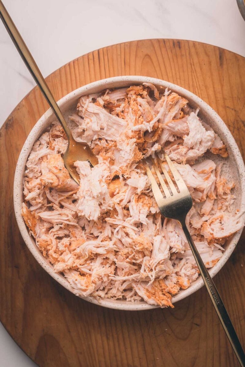 A bowl of shredded chiptole chicken with two forks on a wooden board, photographed from above.