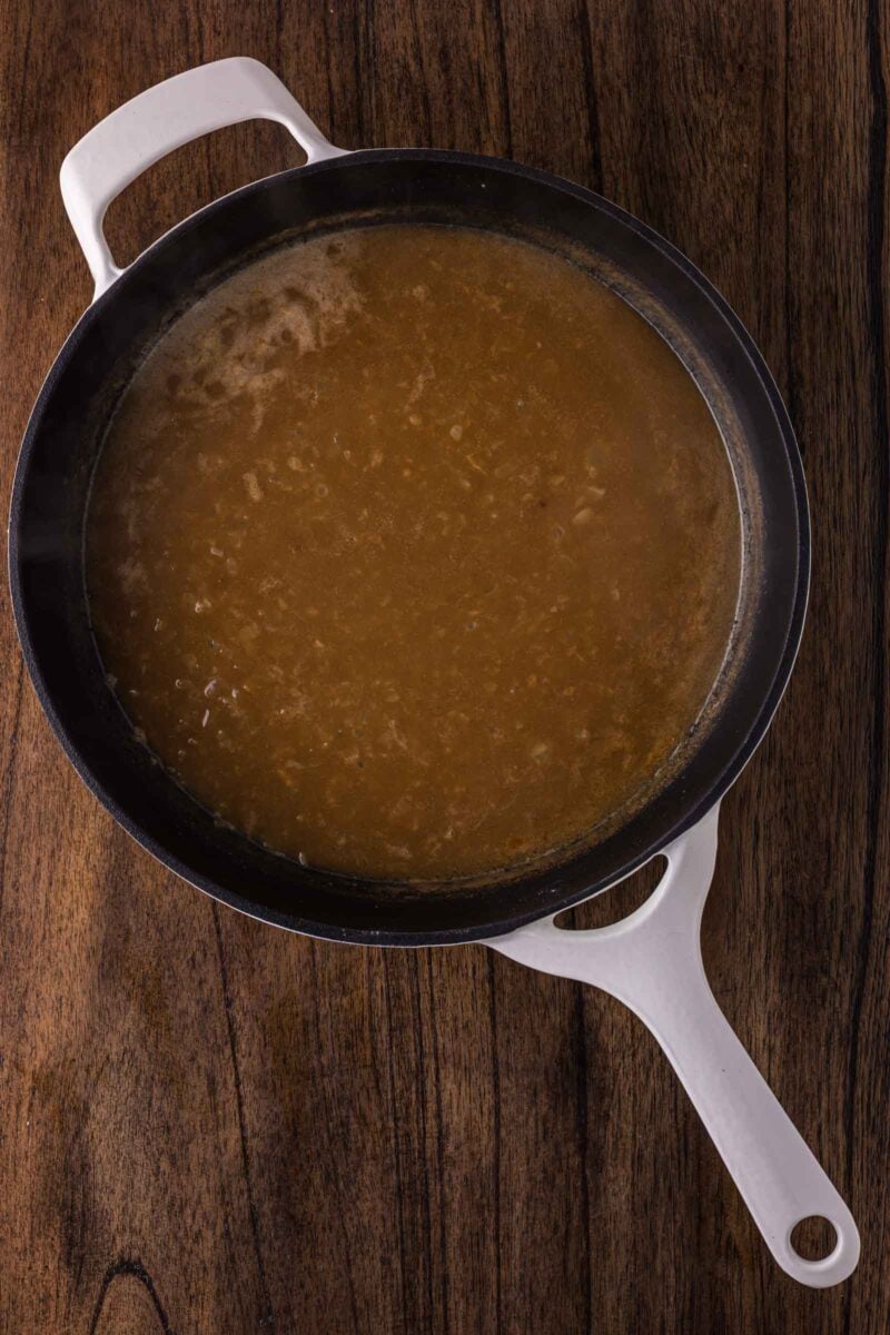 A white-handled skillet filled with brown gravy sits on a wooden surface.