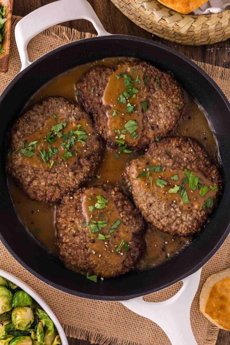 Four cooked country fried steaks with brown gravy and chopped parsley are arranged in a black skillet.