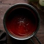 Apple butter BBQ sauce simmered smooth and glossy in the saucepan, thick enough to coat a wing, with apples in the background.