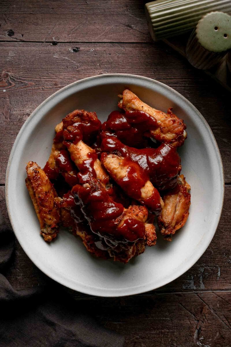 Warm apple butter BBQ sauce poured over a bowl of crisp baked chicken wings, before they get tossed to coat.