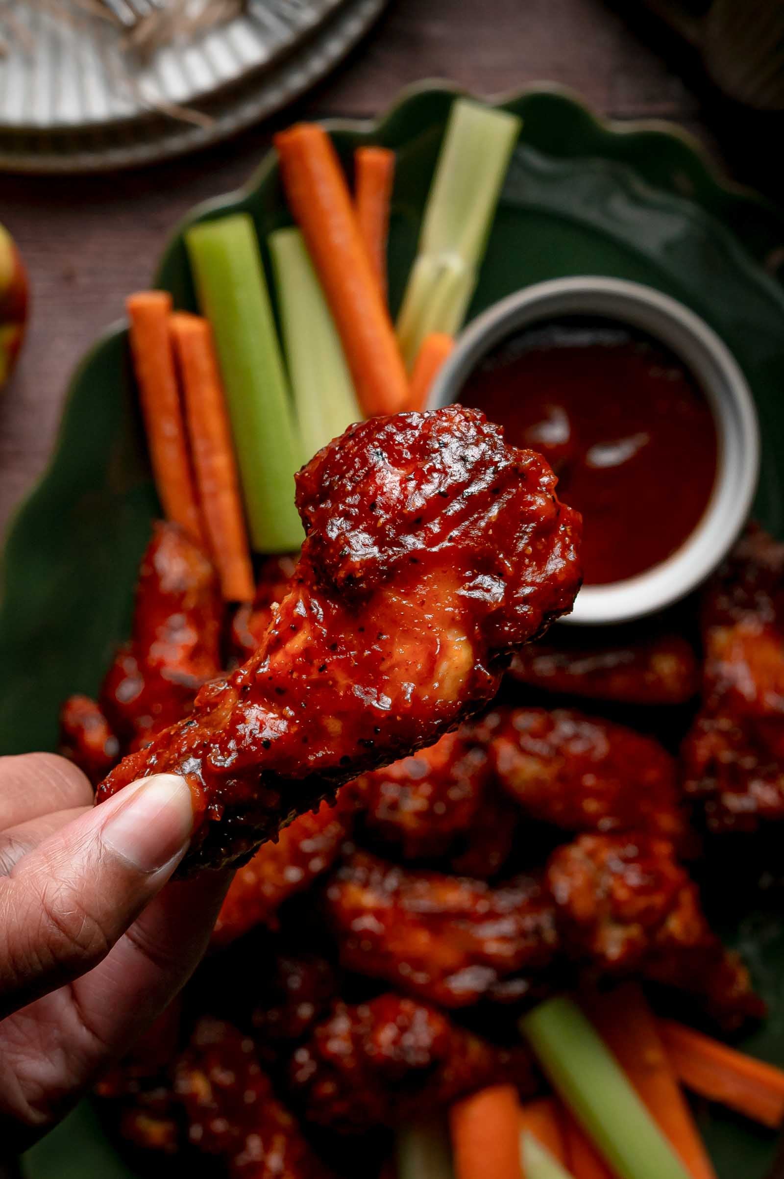 A glazed apple butter BBQ wing held up over the platter, the sauce set and shining on the crisp skin.
