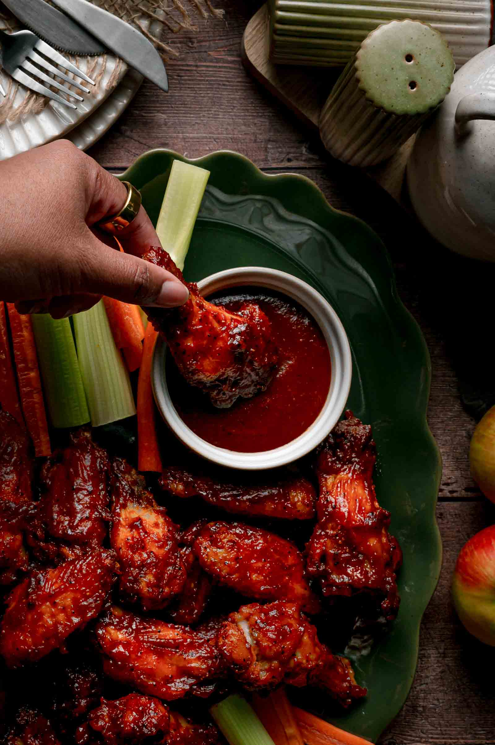 A hand dipping an apple butter BBQ wing into the ramekin of reserved sauce on the green platter.