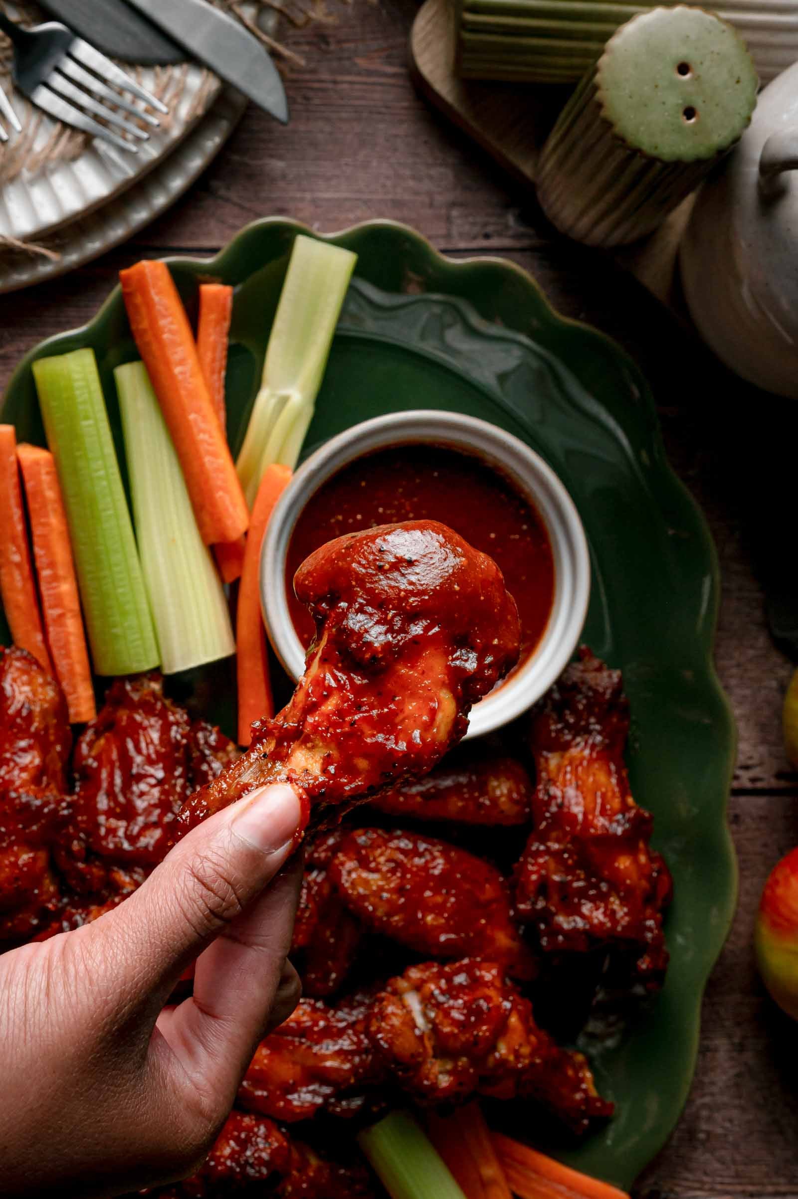 An apple butter BBQ wing lifted dripping from the ramekin of sauce, the rest of the loaded platter below.