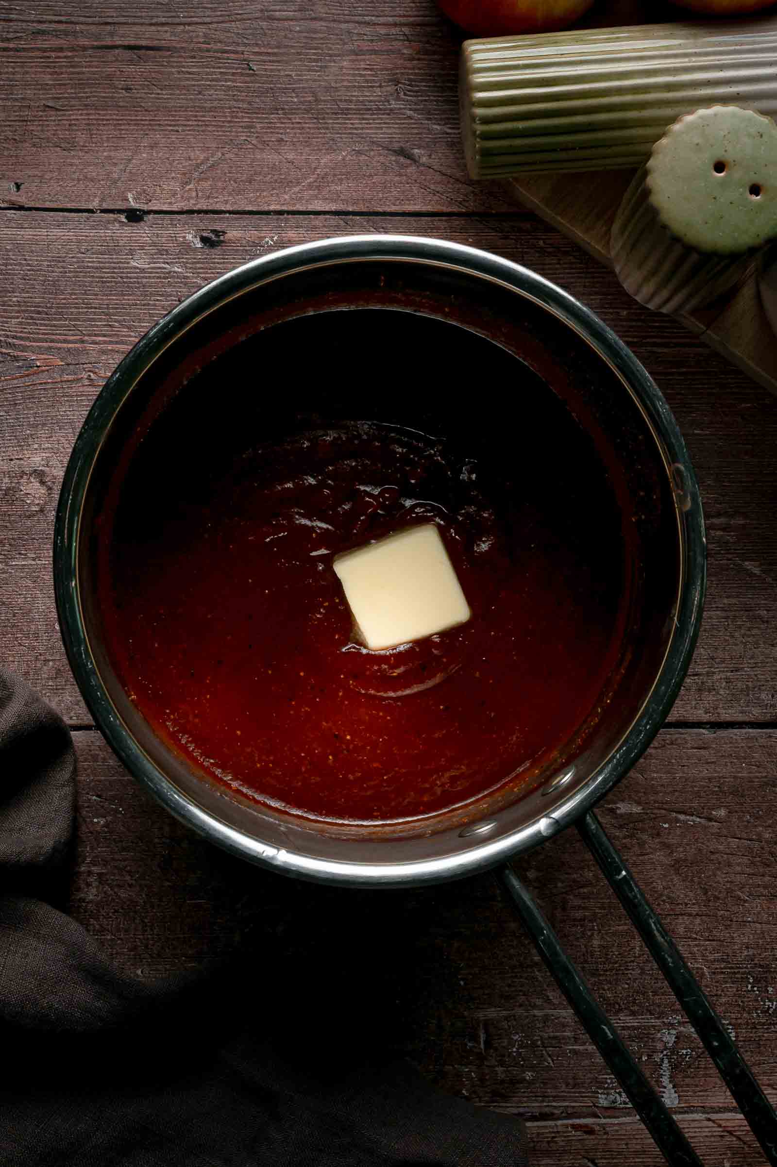 The apple butter BBQ sauce off the heat with a pat of butter melting into the surface, the step that makes it glossy.