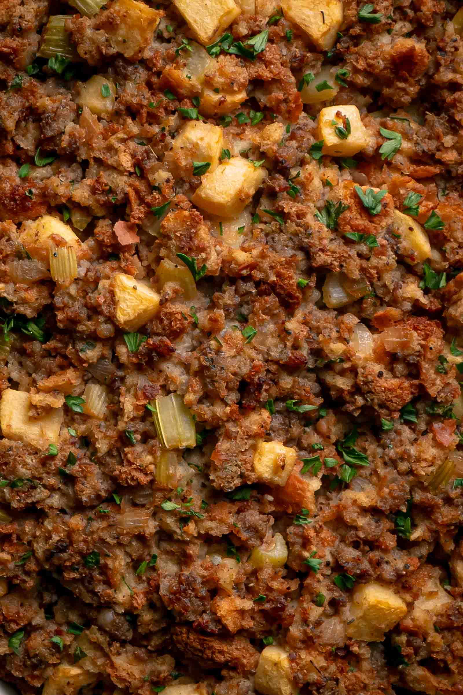 Close up of baked apple sausage stuffing showing browned sausage, chunks of apple, celery and crisp bread edges.