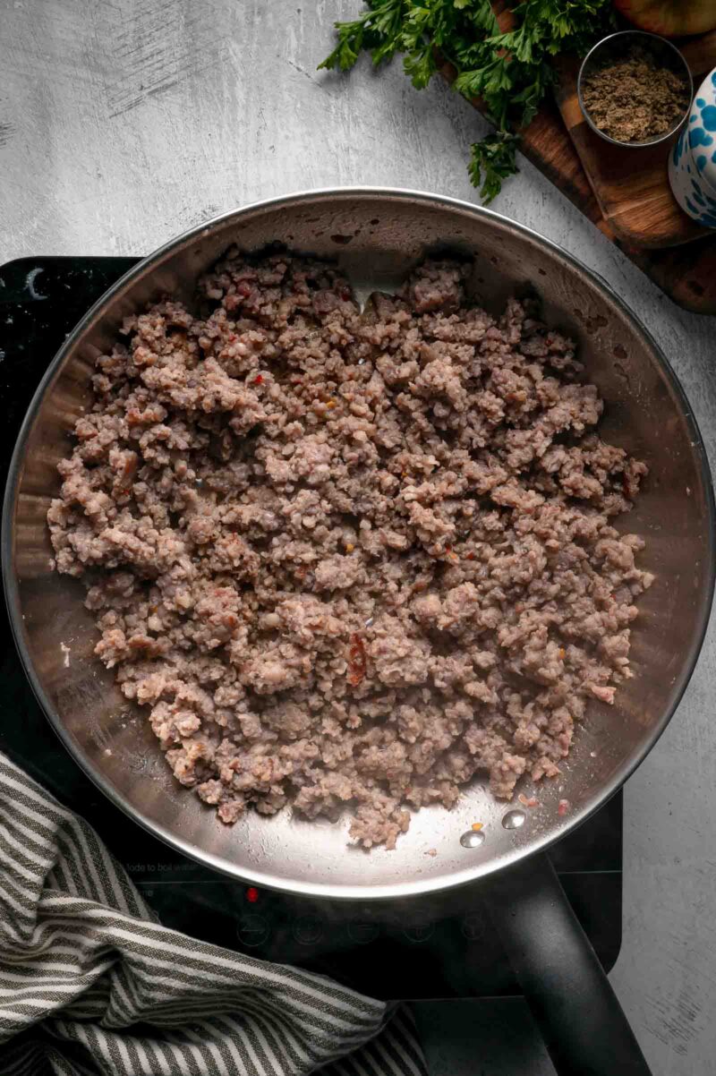 Sage pork sausage browned into crumbles in a stainless steel skillet, with only a thin slick of rendered fat left behind.