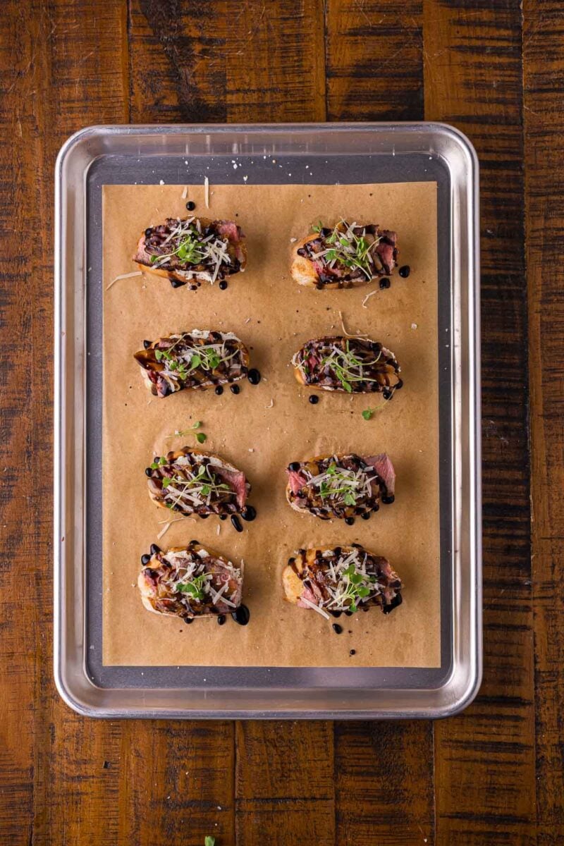 The finished steak crostini on the sheet pan, showered with shaved Parmesan and microgreens over the balsamic.