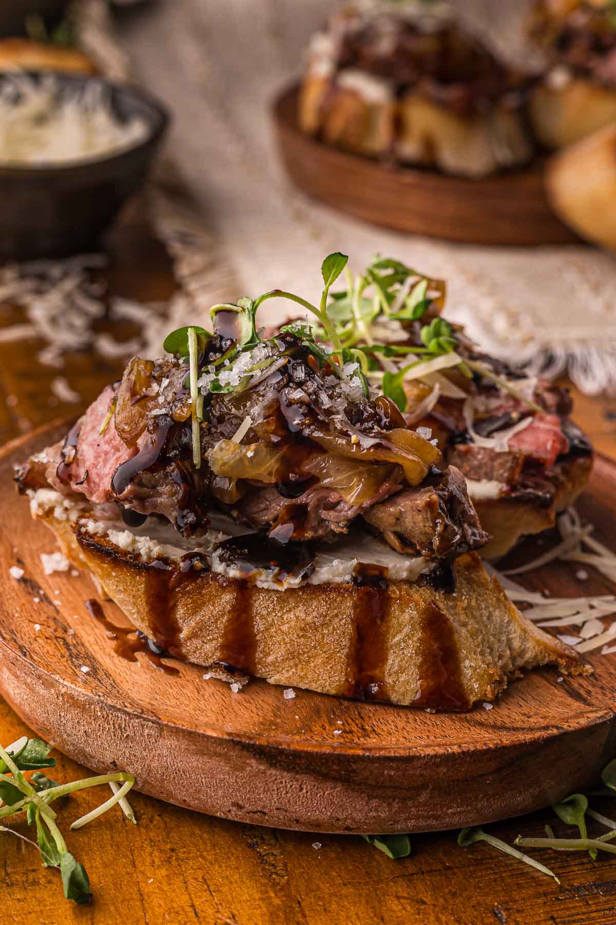Steak crostini on a wood plate with flaky salt over the top, caramelized onions and balsamic layered on garlic herb Boursin.