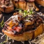 Close up of one steak crostini on slate, the seared crust and pink center of the NY strip visible above the Boursin.