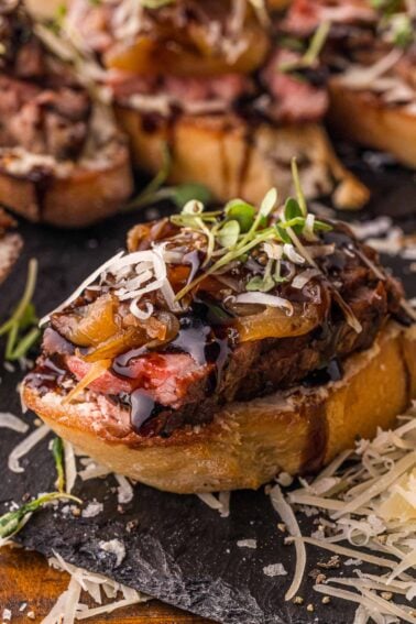 Close up of one steak crostini on slate, the seared crust and pink center of the NY strip visible above the Boursin.