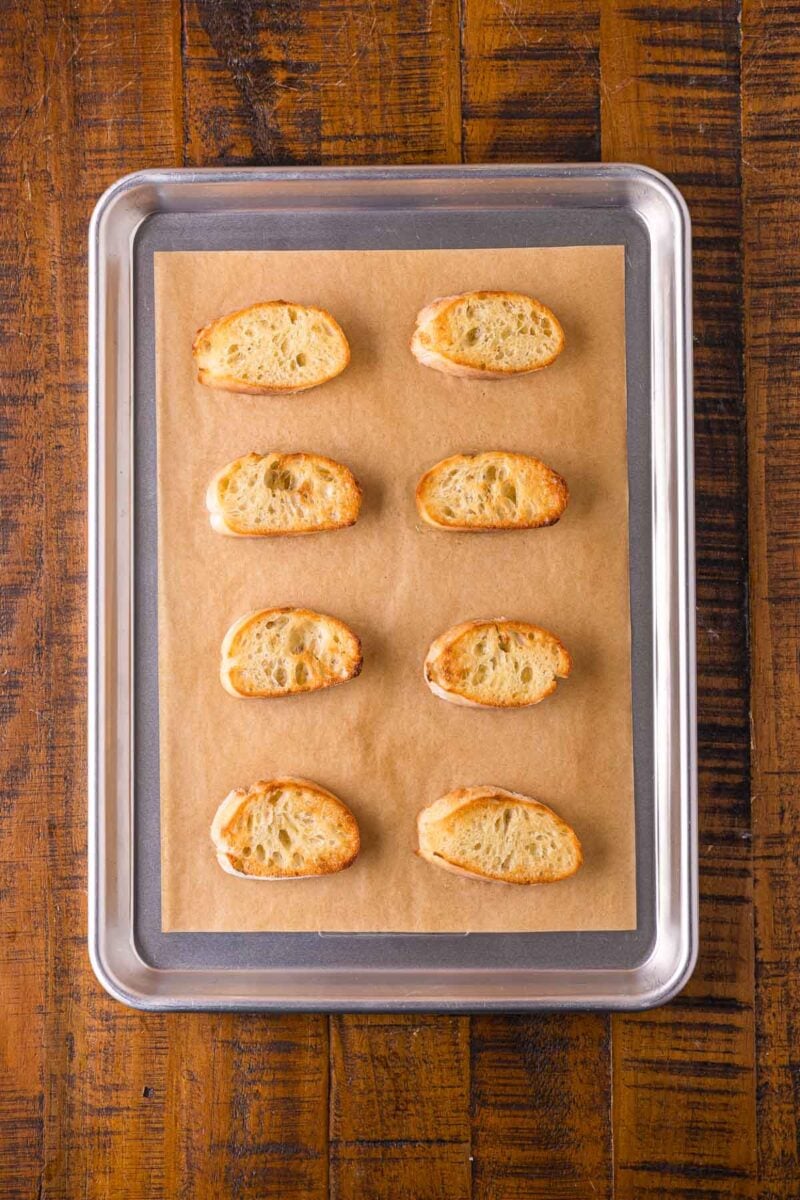 The same baguette rounds after toasting, golden and crisp at the edges on the parchment lined sheet pan.