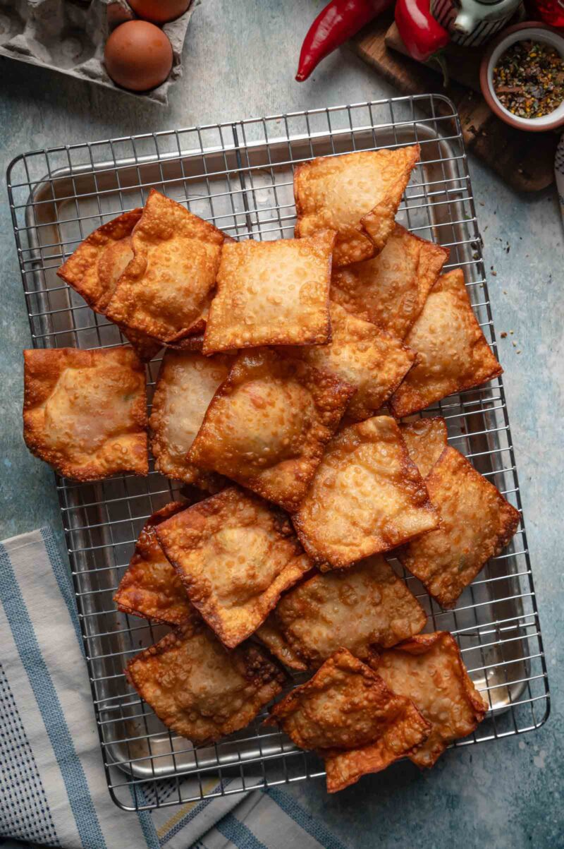 Fried crab rangoon crisps draining on a wire rack set over a sheet pan.
