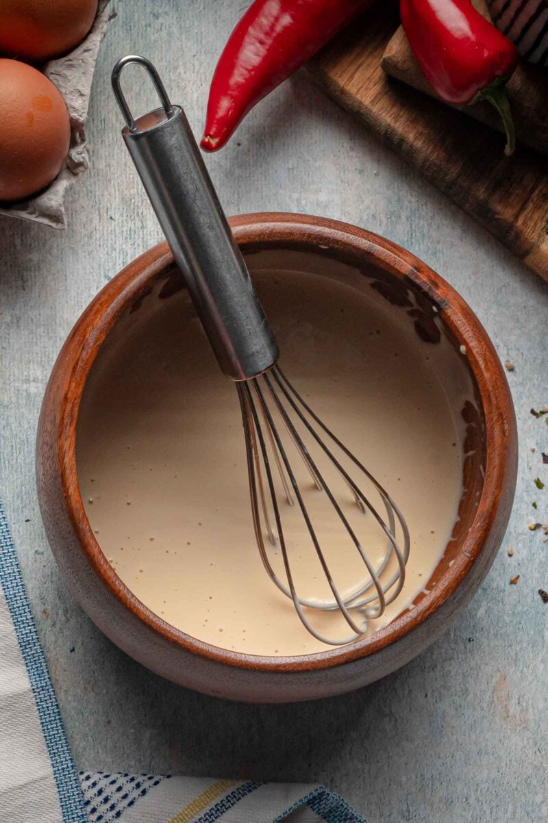 The drizzle sauce whisked smooth and pale in a wooden bowl, whisk resting in the bowl.