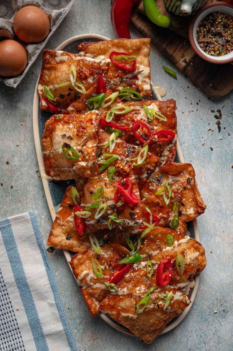 Crab rangoon nachos finished on the platter with sliced red and green chilies and scallions scattered over the drizzle.