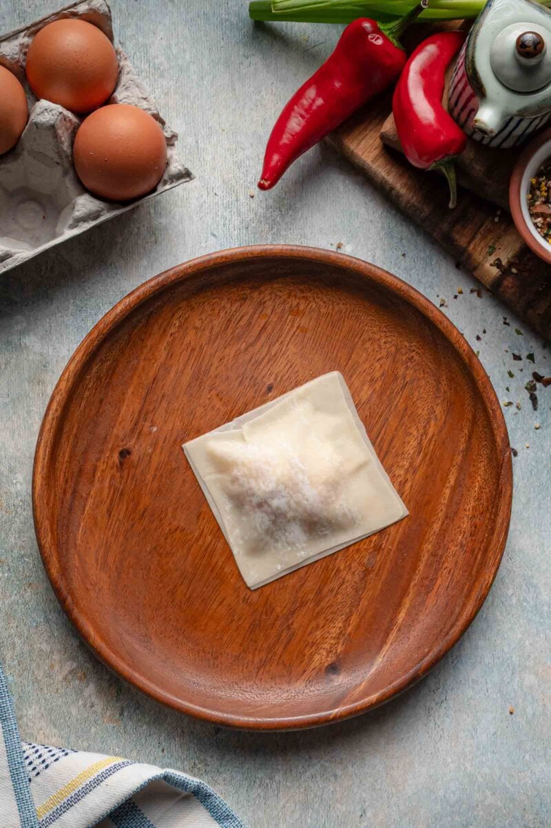 A second wonton wrapper pressed over the filling and sealed into a flat square packet, ready for the fryer.