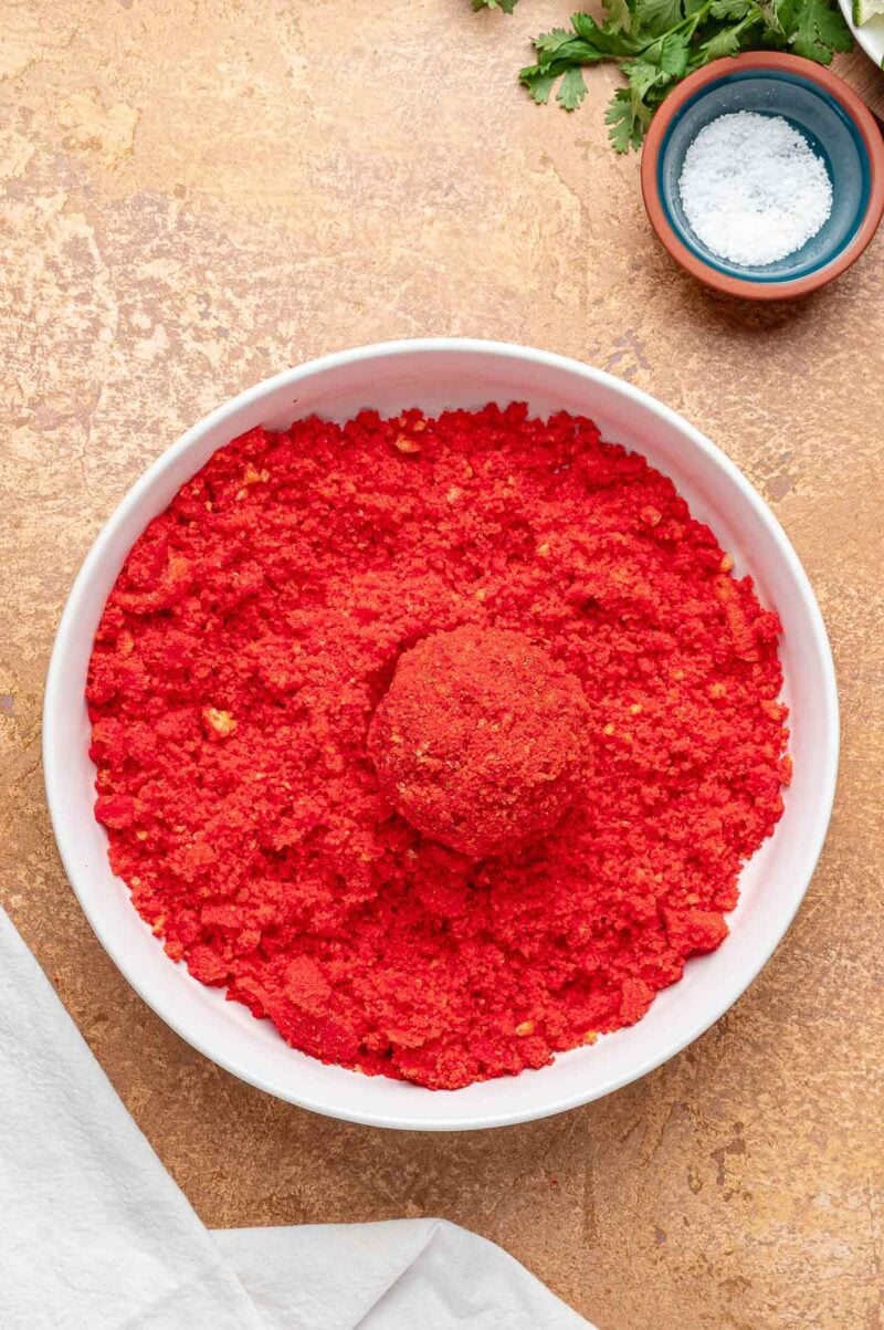 A birria ball fully coated in crushed Hot Cheetos, sitting in the bowl of crumbs and ready for the fryer.