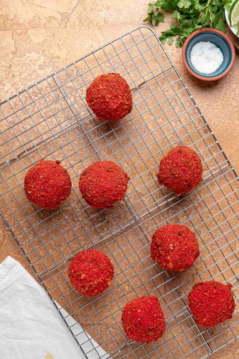 Eight fried birria balls draining on a wire rack so the bottoms of the Hot Cheeto crust stay crisp.