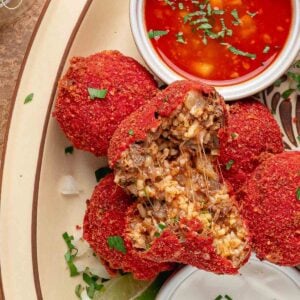 Hot Cheeto birria balls close up, one pulled open with cheese stretching between the halves, next to a ramekin of birria consomé.