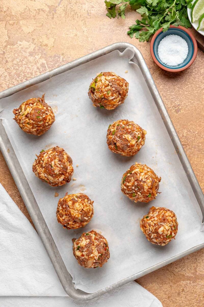Eight raw birria balls rolled and set on a parchment lined sheet pan, ready for a short freeze so they hold their shape.