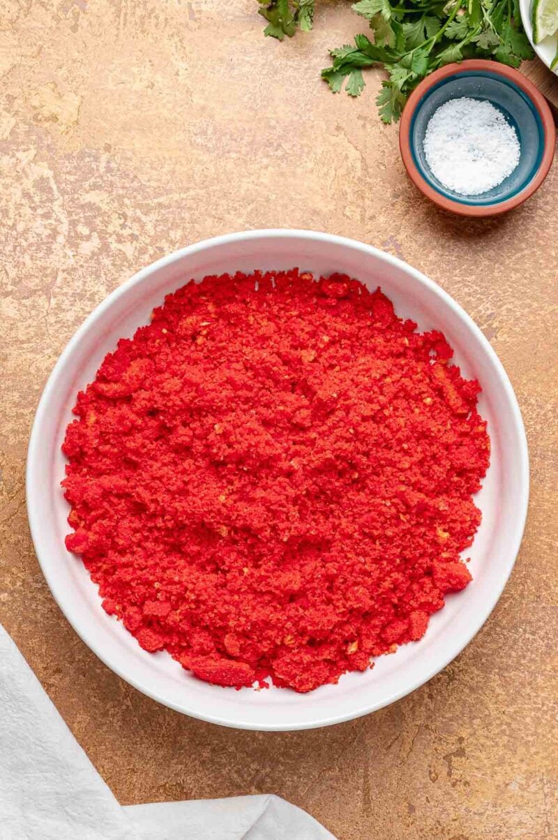 A shallow bowl of finely crushed Hot Cheetos, the coating that gives birria balls their bright red crust.