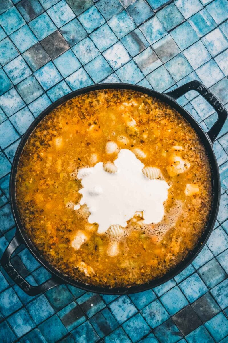 Heavy cream poured into the center of the pot of broth and potato gnocchi, turning the soup creamy.