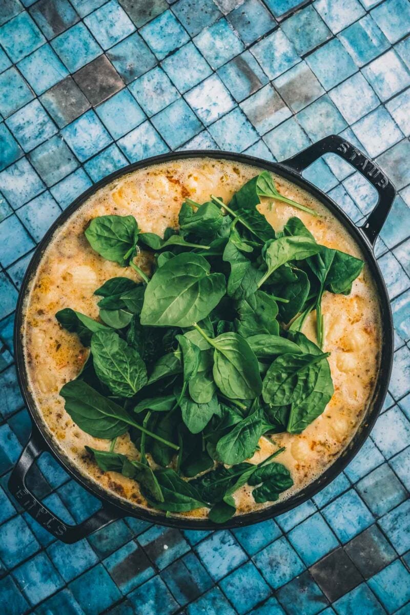 Fresh baby spinach piled on top of the creamy chicken gnocchi soup, ready to wilt into the pot.