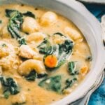 A close bowl of chicken gnocchi soup, potato gnocchi and spinach with a sliced carrot coin in the creamy broth.
