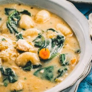 A close bowl of chicken gnocchi soup, potato gnocchi and spinach with a sliced carrot coin in the creamy broth.