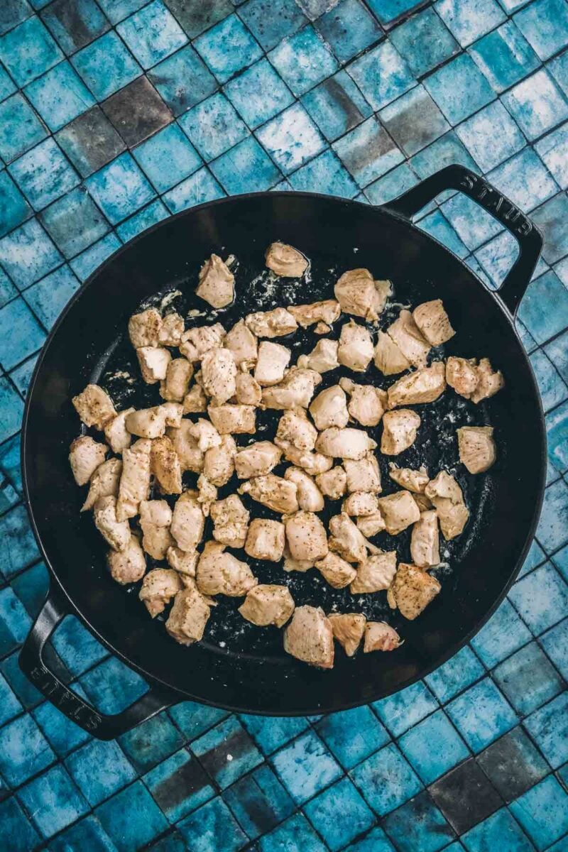 Diced chicken seared golden on the outside in the black braiser, browned for color before it comes out of the pan.