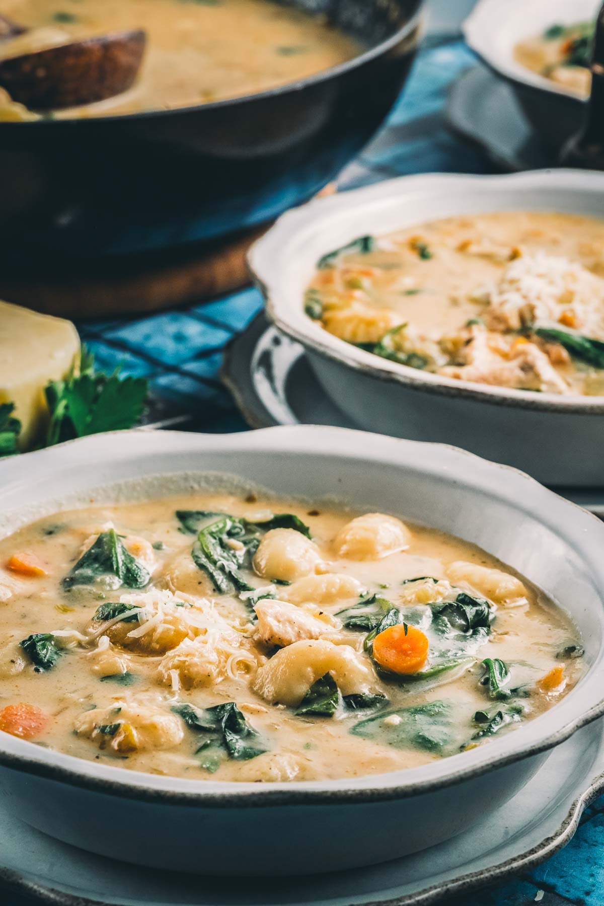 Two bowls of Italian chicken gnocchi soup served from the pot, with a wedge of parmesan and fresh spinach alongside.
