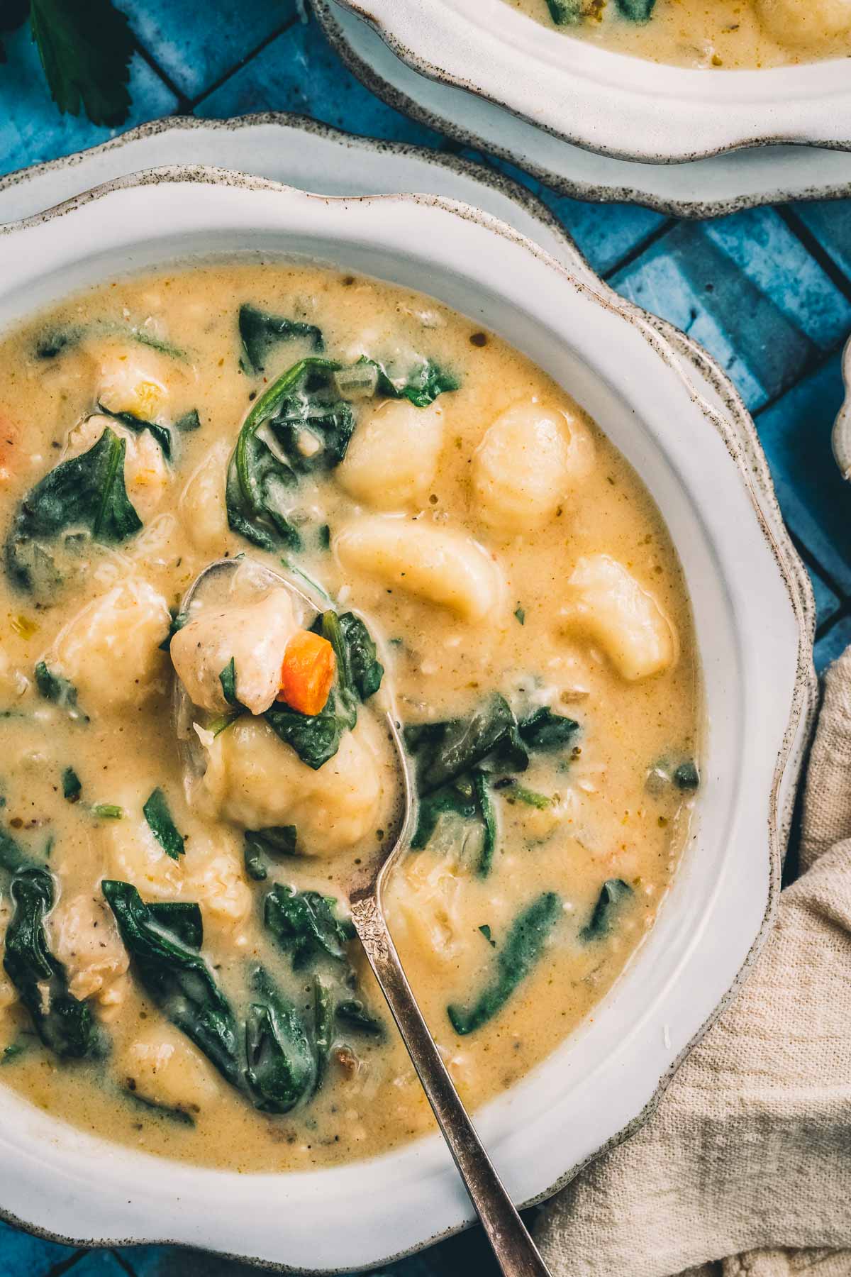 An overhead bowl of Italian chicken gnocchi soup with a spoon resting in the creamy broth, gnocchi, spinach and carrot.