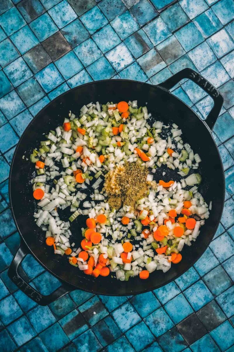 A mound of dried Italian herbs and spices over the diced onion, carrot and celery softening in the black pan.